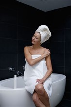 Mature woman sitting in bathroom wrapped in towel. Photo : Rob Lewine