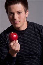 Portrait of teenage boy (16-17) with red apple, studio shot. Photo : Rob Lewine