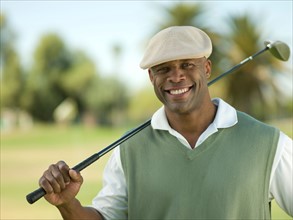 Smiling man on golf course holding golf club. Photo : db2stock