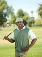 Smiling man on golf course holding golf club. Photo : db2stock