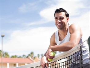 Smiling man standing near tennis net. Photo: db2stock