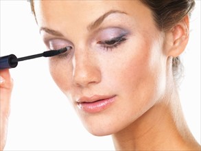 Studio portrait of beautiful brunette applying mascara. Photo : momentimages
