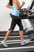 Low section of woman walking on treadmill.