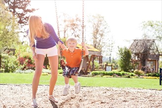USA, Washington State, Seattle, Mother and son (2-3) swinging on swing in park. Photo: Take A Pix