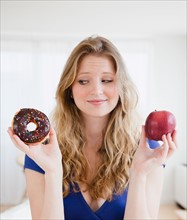 Young woman choosing between donut and apple. Photo: Jamie Grill