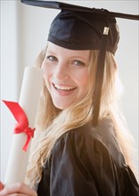 Young woman wearing graduation gown with diploma. Photo : Jamie Grill