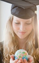 Woman wearing graduation gown holding small globe. Photo : Jamie Grill