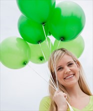 Portrait of young woman holding green balloons. Photo : Jamie Grill
