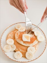 Close up of woman's hands and pancakes with banana. Photo : Jamie Grill
