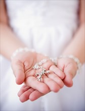Close up of girl's (8-9) hands holding rosary beads. Photo: Jamie Grill