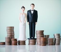 Close up of wedding cake figurines on stacks of coins. Photo : Jamie Grill