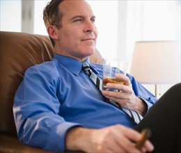 Businessman relaxing with drink and cigar. Photo : Jamie Grill