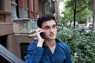 USA, New York, New York City, Young man talking on mobile phone on street. Photo : Winslow