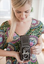 Young woman holding antique camera. Photo : Jamie Grill