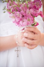 Close up of girl's (8-9) hands holding flowers and rosary beads. Photo: Jamie Grill