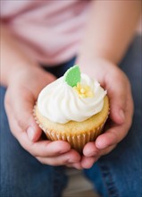 Close up of girl's (8-9) hands holding cupcake. Photo: Jamie Grill