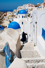 Greece, Cyclades Islands, Santorini, Oia, Woman descending steps past traditional buildings.