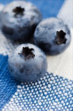 Three blueberries on tablecloth.