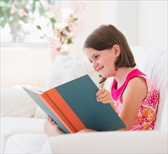 Close up of girl (6-7) reading book on sofa. Photo : Daniel Grill