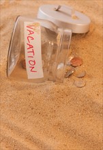 Close up of jar with coins spilled on sand. Photo: Daniel Grill