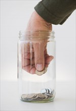 Hand inserting coin into jar.