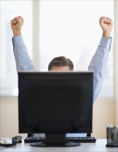Businessman raising hands from behind computer.