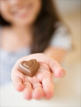 Close up of girl's (10-11) hand holding chocolate heart. Photo : Jamie Grill