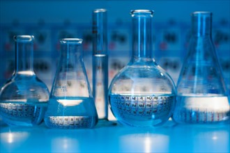 Beakers and flasks with periodic tables in laboratory.