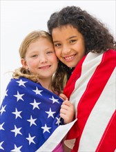 Portrait of girls (8-9) wrapped in US flag.