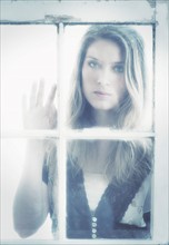 Portrait of young woman looking through window.