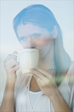 Pensive woman drinking tea, looking through window.