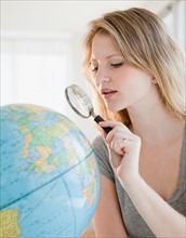 Young woman with magnifying glass searching on globe. Photo : Jamie Grill