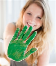 Young woman with hand covered with green paint. Photo : Jamie Grill