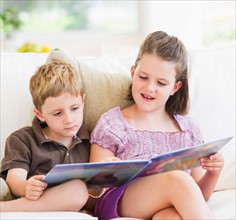 Close up of girl (6-7) and boy (4-5) reading book on sofa. Photo : Daniel Grill