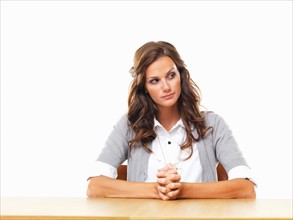 Concerned business woman sitting at table with hands clasped. Photo : momentimages