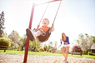 USA, Washington State, Seattle, Mother and son (2-3) swinging on swing in park. Photo : Take A Pix
