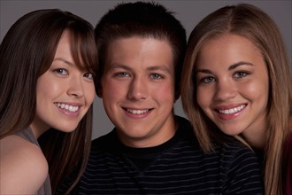 Portrait of teenage boy (16-17) and girl (16-17) with young friend, studio shot. Photo : Rob Lewine