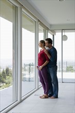 Mature couple in empty living room looking through window. Photo : Rob Lewine