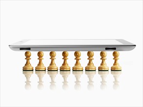 Digital tablet on wooden chess pawns, studio shot. Photo: David Arky