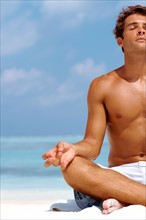 Cropped image of a young man meditating at the beach in a lotus position. Photo: momentimages