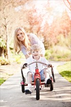 Mother and son (2-3) riding tricycle in park. Photo : Take A Pix Media