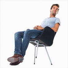Studio shot of young man balancing on chair. Photo : momentimages