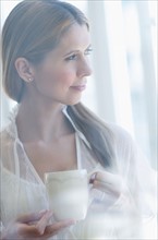 Pensive woman holding tea, looking through window.