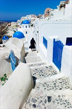 Greece, Cyclades Islands, Santorini, Oia, Woman walking down steps in town.