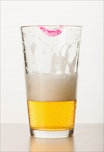 Studio shot of beer glass with lipstick mark on edge.