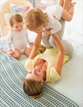 Mother playing with daughters (2-3) on bed.