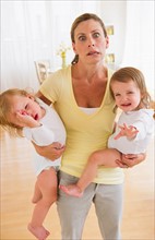 Mother holding crying daughters (2-3) and making facial expression.