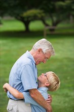 Grandfather and grandson (10-11) embracing in park.