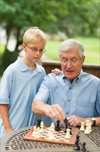 Grandfather teaching grandson (10-11) how to play chess.