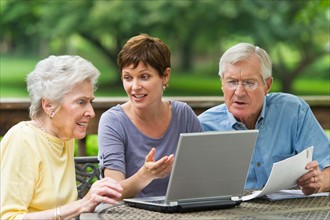 Senior parents and adult daughter using laptop on porch.